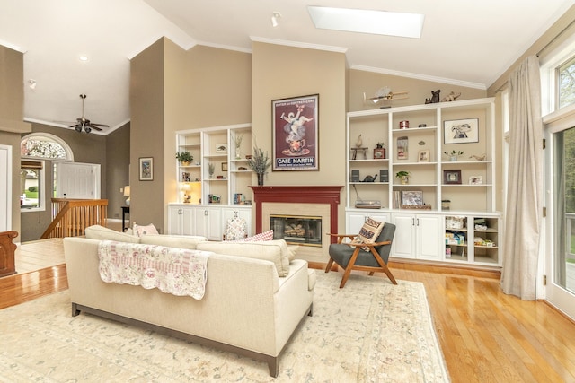 70 Chestnut Ct, Chelsea, MI 48118 - living room with a glass covered fireplace, ornamental molding, light wood finished floors, a ceiling fan, and a skylight