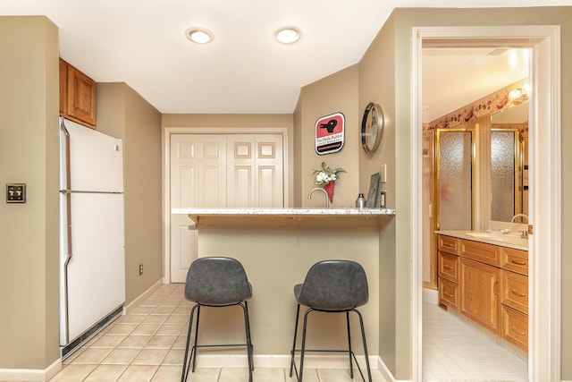 70 Chestnut Ct, Chelsea, MI 48118 - kitchen featuring a kitchen bar, brown cabinets, freestanding refrigerator, and light countertops
