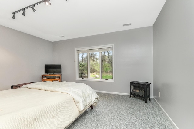 70 Chestnut Ct, Chelsea, MI 48118 - carpeted bedroom featuring rail lighting, visible vents, a wood stove, and baseboards