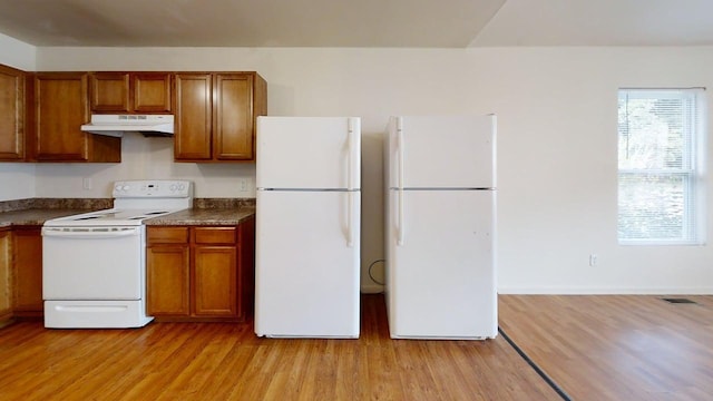 kitchen featuring under cabinet range hood, white appliances, brown cabinets, and dark countertops