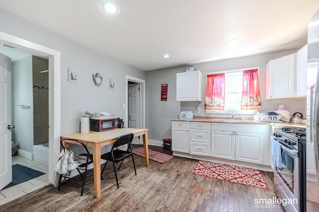 kitchen featuring black microwave, light wood-type flooring, light countertops, white cabinetry, and gas stove