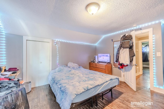 bedroom featuring a closet, lofted ceiling, a textured ceiling, and light wood finished floors