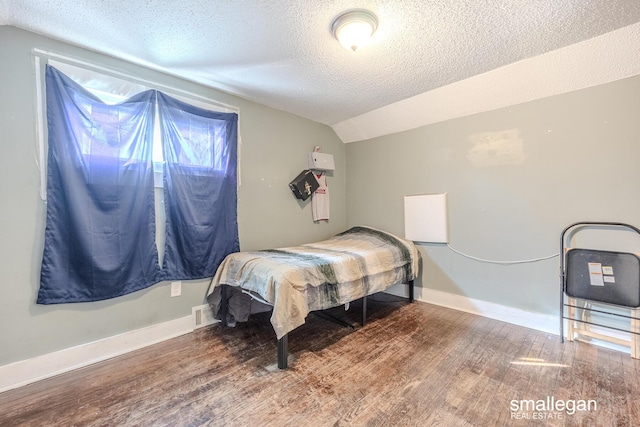 bedroom featuring vaulted ceiling, wood finished floors, a textured ceiling, and baseboards