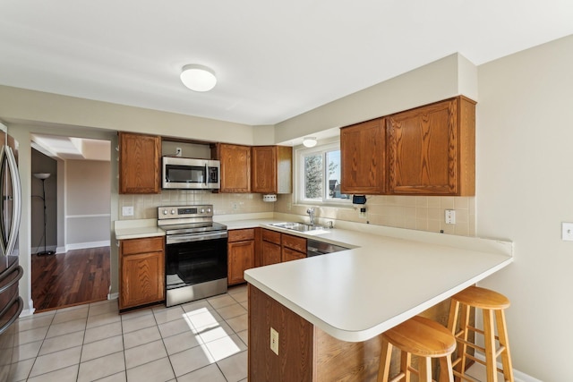 4658 White Pine Ct, Ypsilanti, MI 48197 - kitchen with stainless steel appliances, a peninsula, backsplash, brown cabinets, and a breakfast bar area