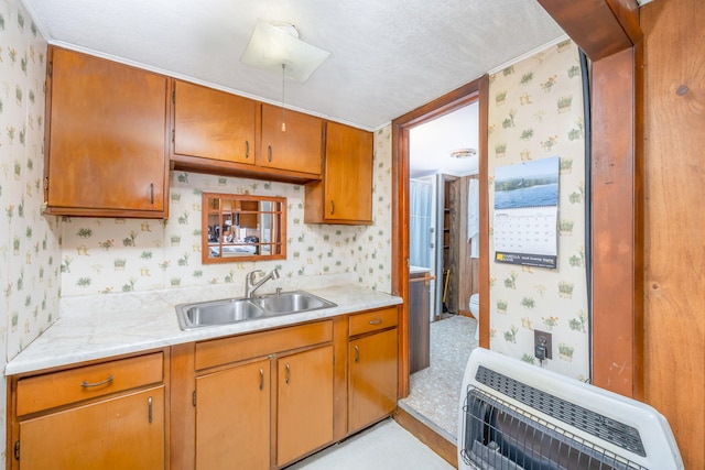 kitchen with a sink, wallpapered walls, heating unit, brown cabinets, and light countertops