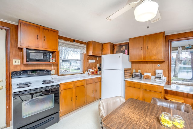kitchen featuring light countertops, freestanding refrigerator, black microwave, brown cabinetry, and electric range