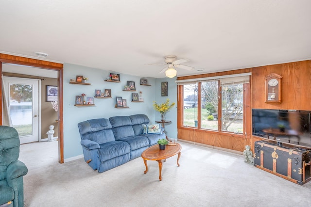 living room featuring baseboards, wooden walls, carpet flooring, and ceiling fan