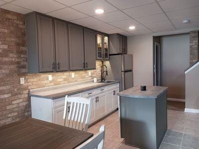 935 Stony Lake Ct, Oxford, MI 48371 - kitchen featuring brick wall, glass insert cabinets, a sink, and freestanding refrigerator
