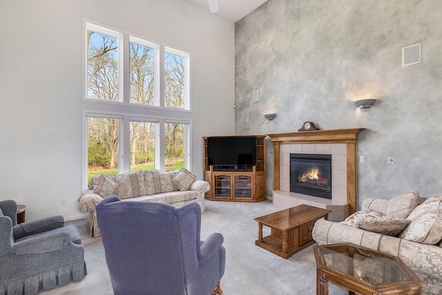 living room with a high ceiling, light carpet, a tiled fireplace, and a healthy amount of sunlight