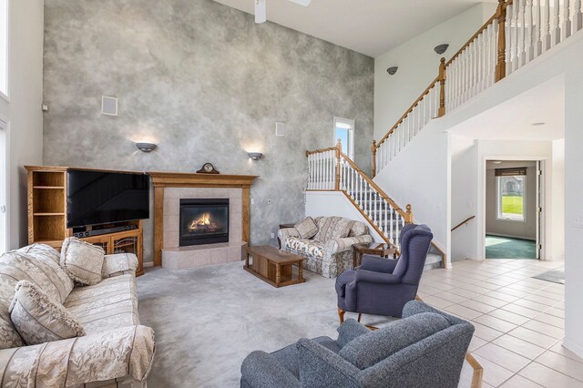 living area featuring stairs, visible vents, a tiled fireplace, and a towering ceiling