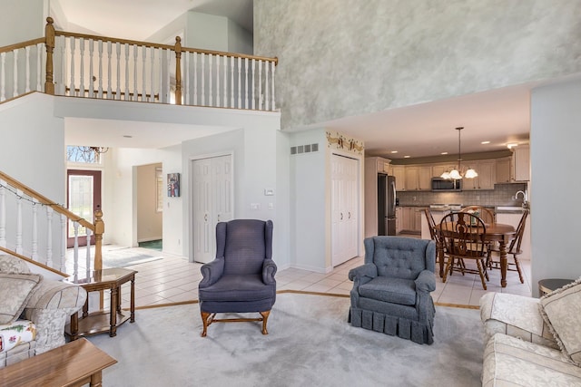 living area featuring a towering ceiling, visible vents, light tile patterned floors, a notable chandelier, and stairs