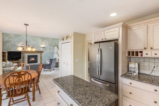 kitchen with light tile patterned flooring, an inviting chandelier, dark stone countertops, freestanding refrigerator, and open floor plan