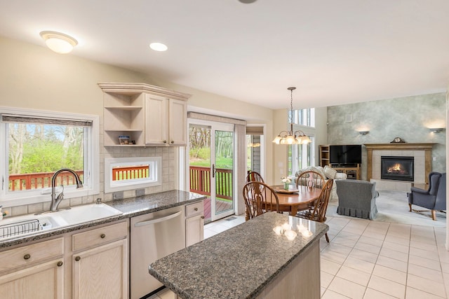 kitchen featuring stainless steel dishwasher, a fireplace, a sink, light tile patterned floors, and open floor plan