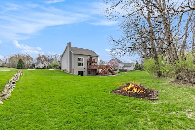 back of house with a chimney, a wooden deck, stairway, a yard, and a fire pit