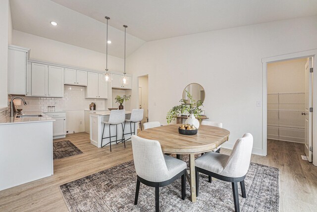 dining space with high vaulted ceiling and light wood-style floors