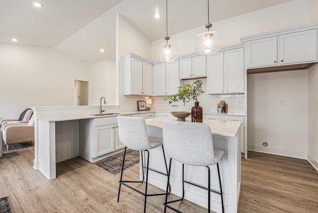 kitchen with a sink, tasteful backsplash, light wood-style floors, lofted ceiling, and light countertops