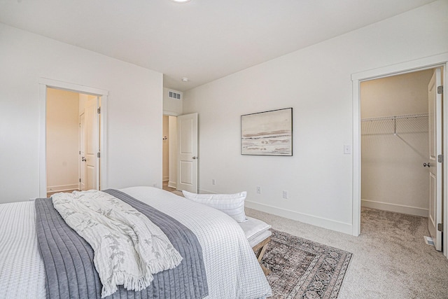 bedroom featuring a closet, a walk in closet, light colored carpet, baseboards, and visible vents