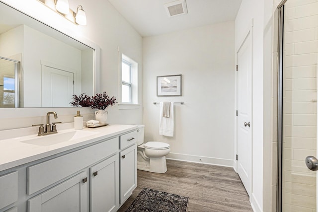 full bath featuring wood finished floors, toilet, vanity, baseboards, and a stall shower