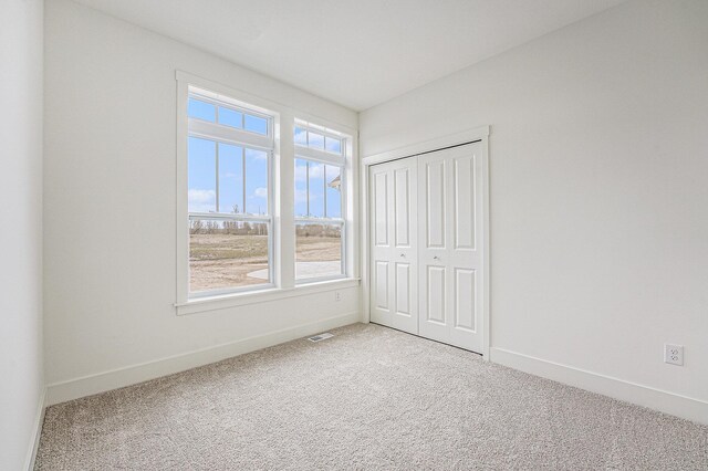 unfurnished bedroom with light carpet, a closet, visible vents, and baseboards