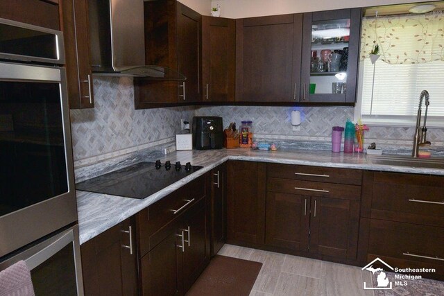 kitchen with oven, a sink, tasteful backsplash, wall chimney range hood, and black electric stovetop