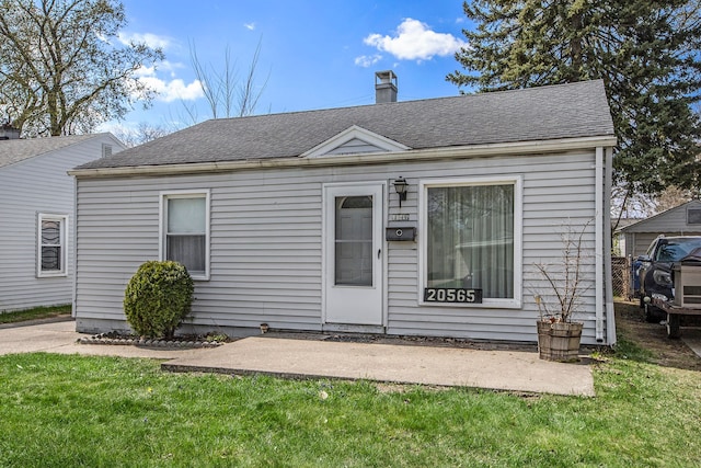 view of front of property featuring a chimney, a patio area, a shingled roof, and a front yard
