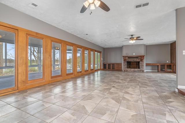 unfurnished living room featuring a ceiling fan, a brick fireplace, a textured ceiling, and visible vents