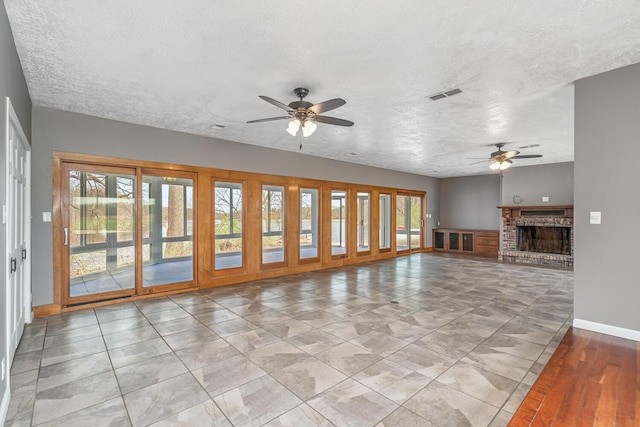 unfurnished living room featuring baseboards, a ceiling fan, visible vents, and a textured ceiling