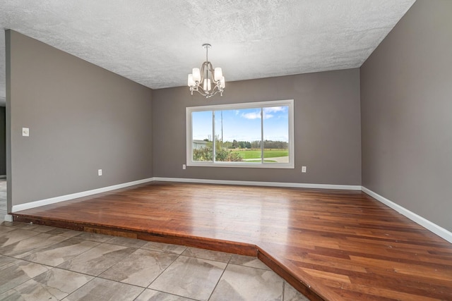 unfurnished room with wood finished floors, baseboards, a textured ceiling, and a chandelier