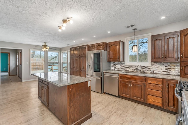 kitchen with a ceiling fan, a center island, a sink, light wood-style flooring, and appliances with stainless steel finishes