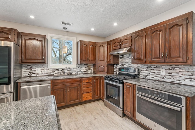 kitchen with stainless steel appliances, light wood-style flooring, a sink, dark stone countertops, and under cabinet range hood