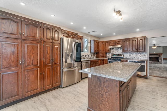 kitchen with a textured ceiling, decorative backsplash, appliances with stainless steel finishes, under cabinet range hood, and a kitchen island
