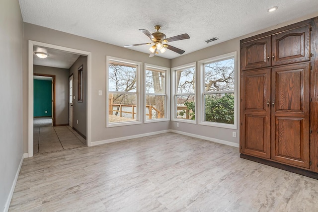 unfurnished room featuring a ceiling fan, light wood finished floors, visible vents, and a healthy amount of sunlight