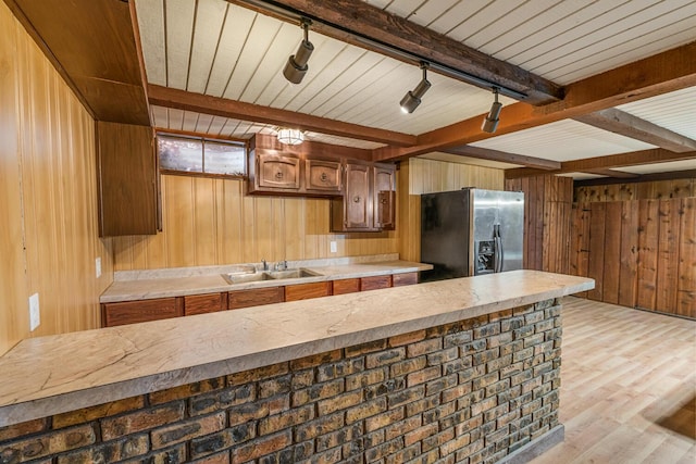 kitchen with wood walls, a sink, light countertops, and stainless steel fridge