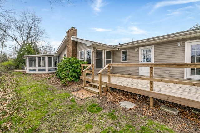 back of property with a wooden deck, a chimney, and a sunroom