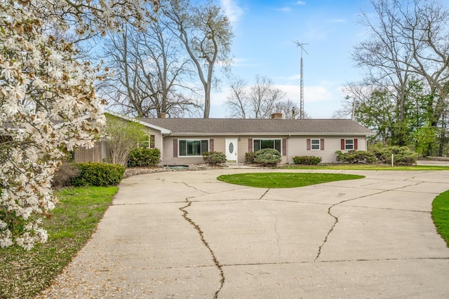 ranch-style home featuring a front lawn, a chimney, and curved driveway