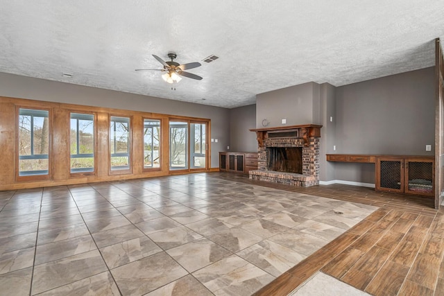 unfurnished living room featuring a textured ceiling, ceiling fan, a fireplace, baseboards, and visible vents
