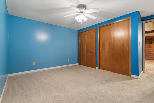 unfurnished bedroom with carpet, multiple closets, baseboards, and ceiling fan