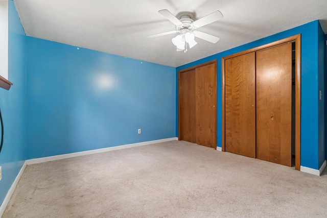 unfurnished bedroom with two closets, ceiling fan, baseboards, and carpet