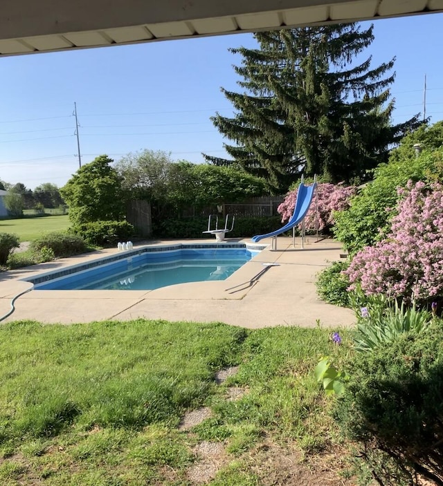 pool featuring a water slide, fence, a patio, and a lawn