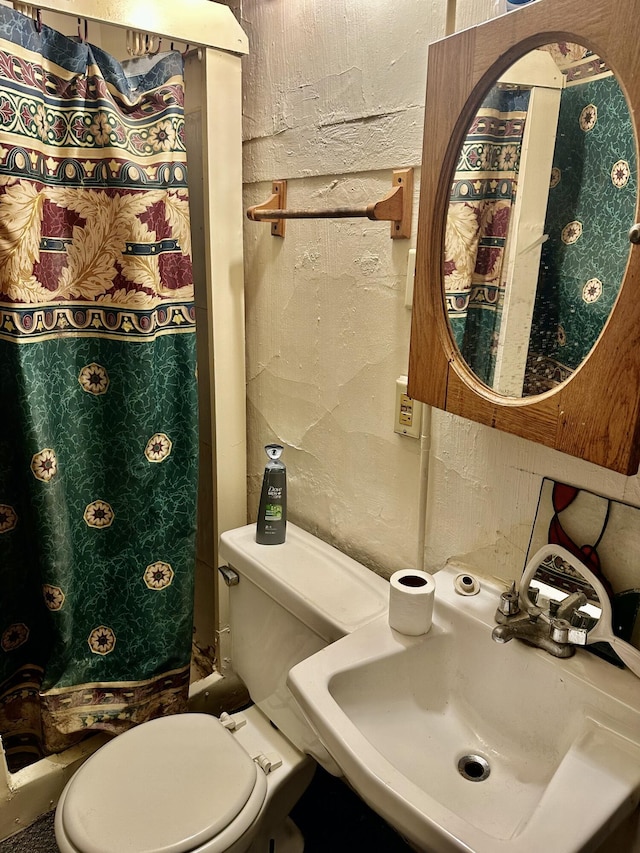 bathroom featuring toilet, a textured wall, a sink, and a shower with shower curtain