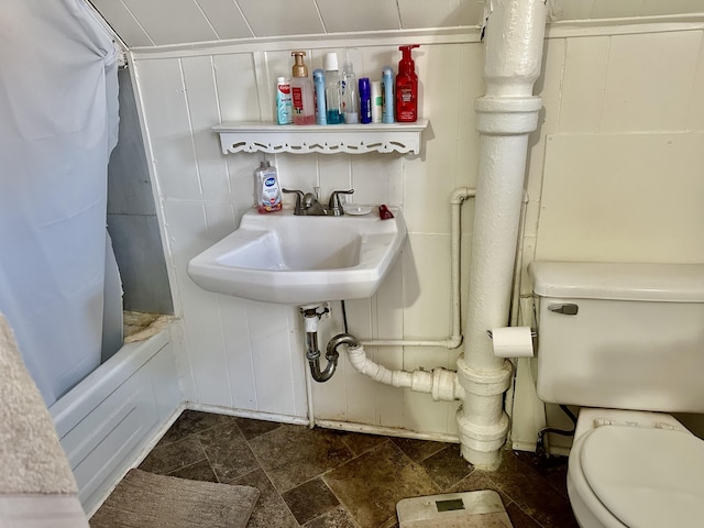 full bath featuring toilet, stone finish floor, and shower / bathtub combination with curtain