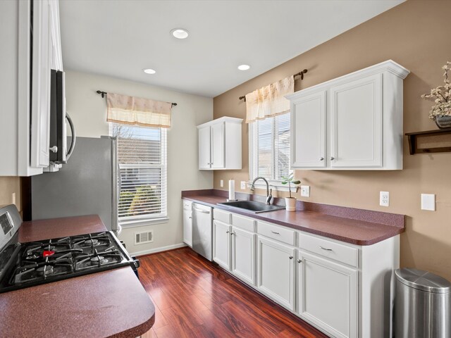 kitchen with a sink, stainless steel appliances, white cabinets, dark wood-style flooring, and visible vents