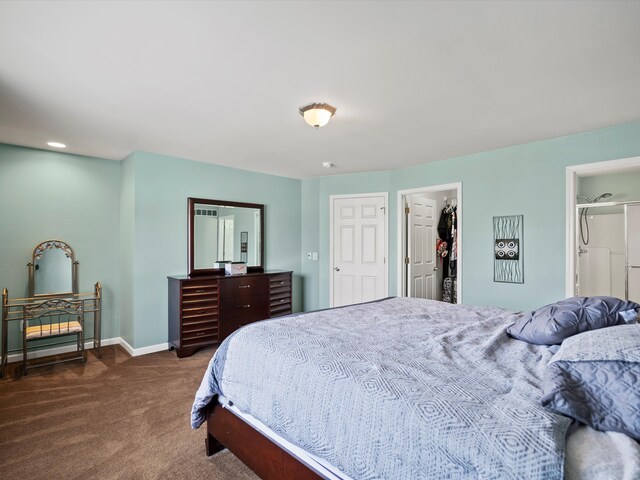 bedroom with a walk in closet, dark carpet, and baseboards