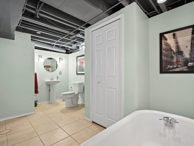 bathroom with a sink, toilet, baseboards, a freestanding tub, and tile patterned flooring