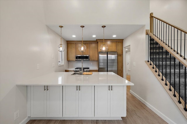 kitchen featuring light wood finished floors, brown cabinets, stainless steel appliances, a peninsula, and baseboards