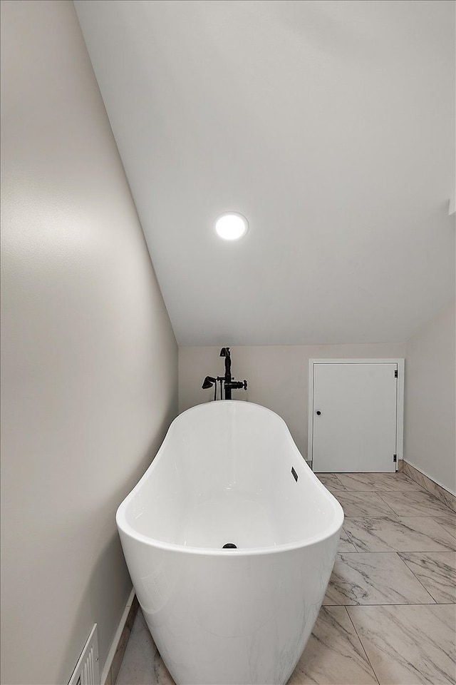 full bathroom featuring marble finish floor, a freestanding bath, and lofted ceiling