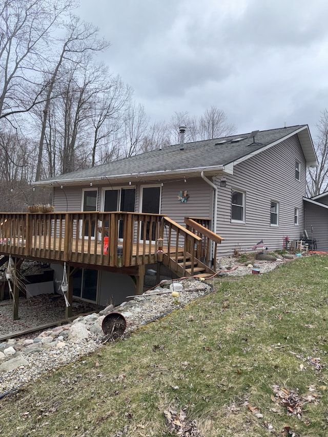 rear view of house with roof with shingles, a wooden deck, and a yard