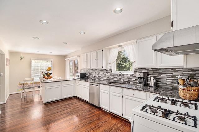 kitchen featuring under cabinet range hood, dishwasher, a sink, white gas stove, and a peninsula