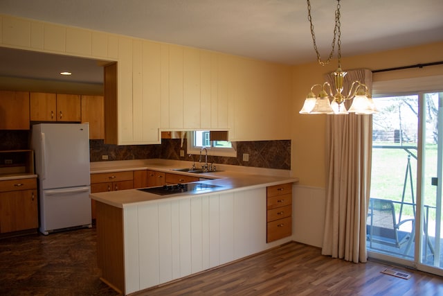 kitchen featuring freestanding refrigerator, a peninsula, light countertops, black electric cooktop, and a sink