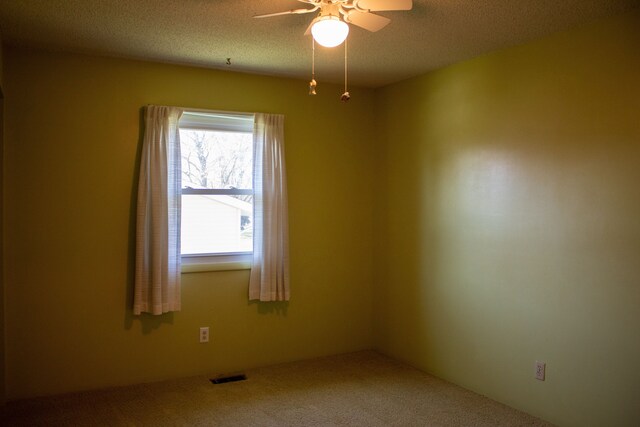 carpeted spare room featuring a ceiling fan, a textured ceiling, and visible vents